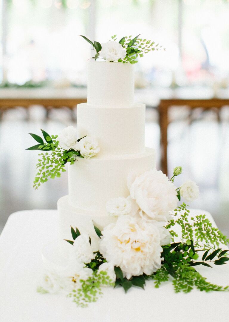 All-white four-tier cake with white flowers and greenery decorations.