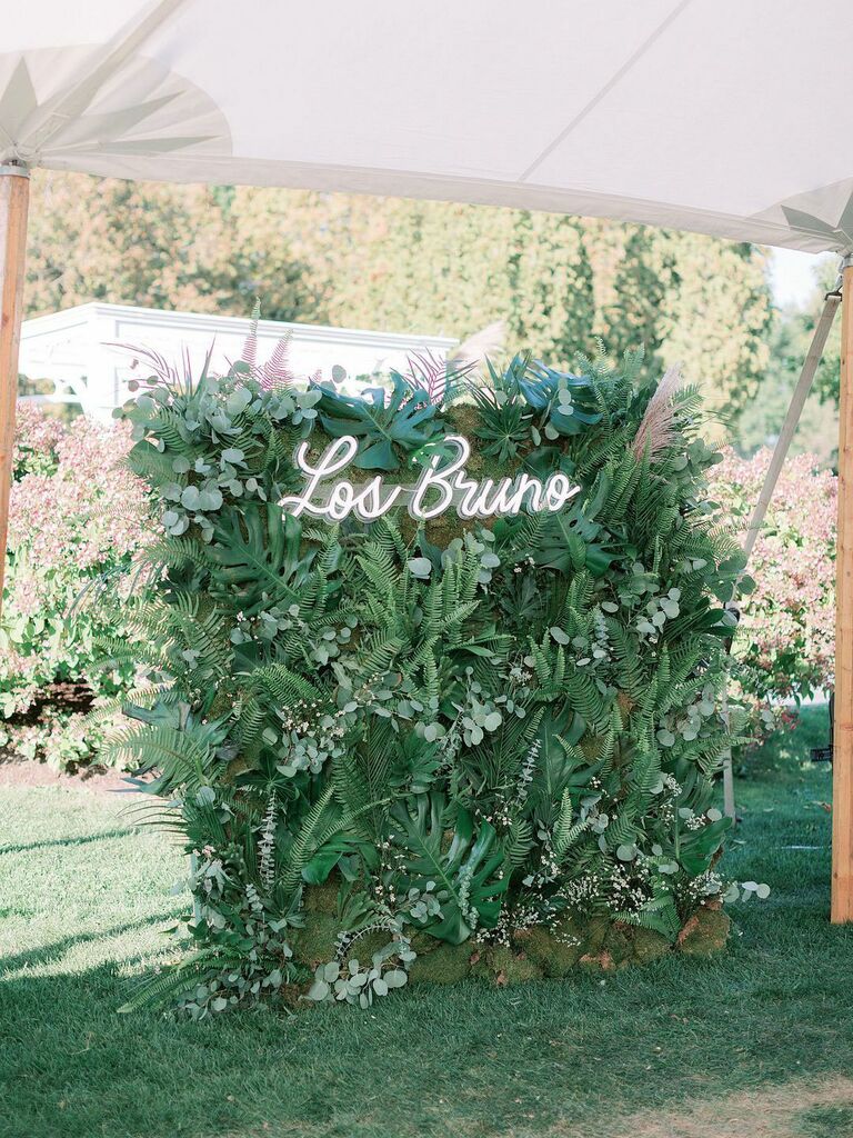 Greenery wall decoration at wedding reception with neon last name sign at top