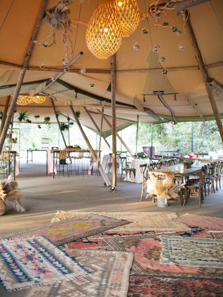 Bohemian tented wedding reception with colorful layered rugs and macrame hanging lights