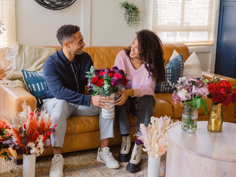 Пара, сидящая на диване, обменивается вазой с цветами