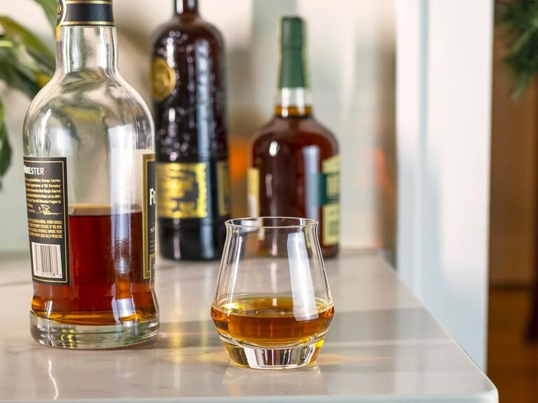 Гладкий изогнутый стакан для виски на столе рядом с бутылкой бурбона