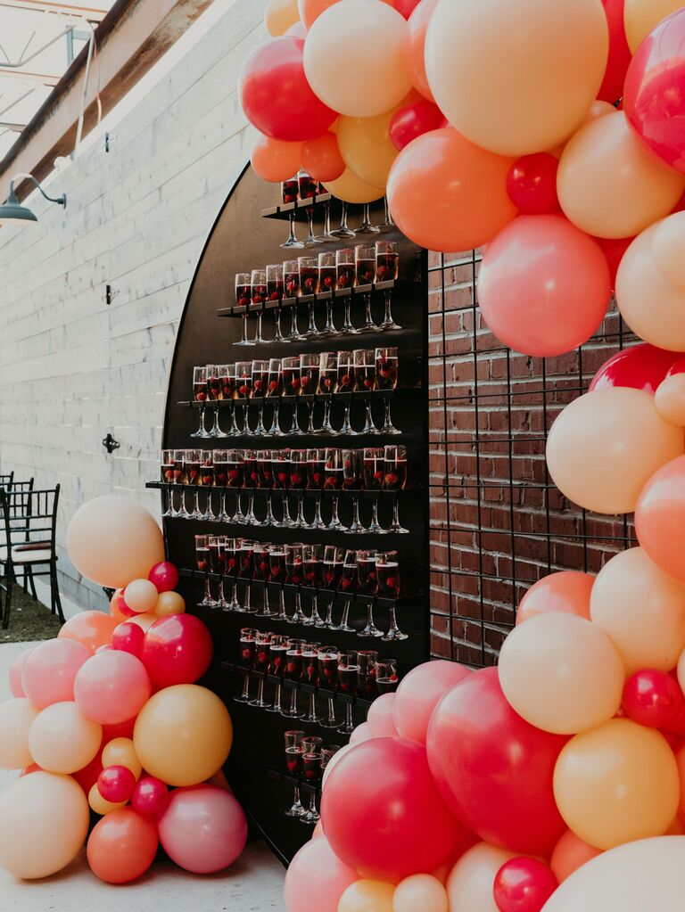 Champagne welcome wall at wedding reception with pink and orange balloon arch